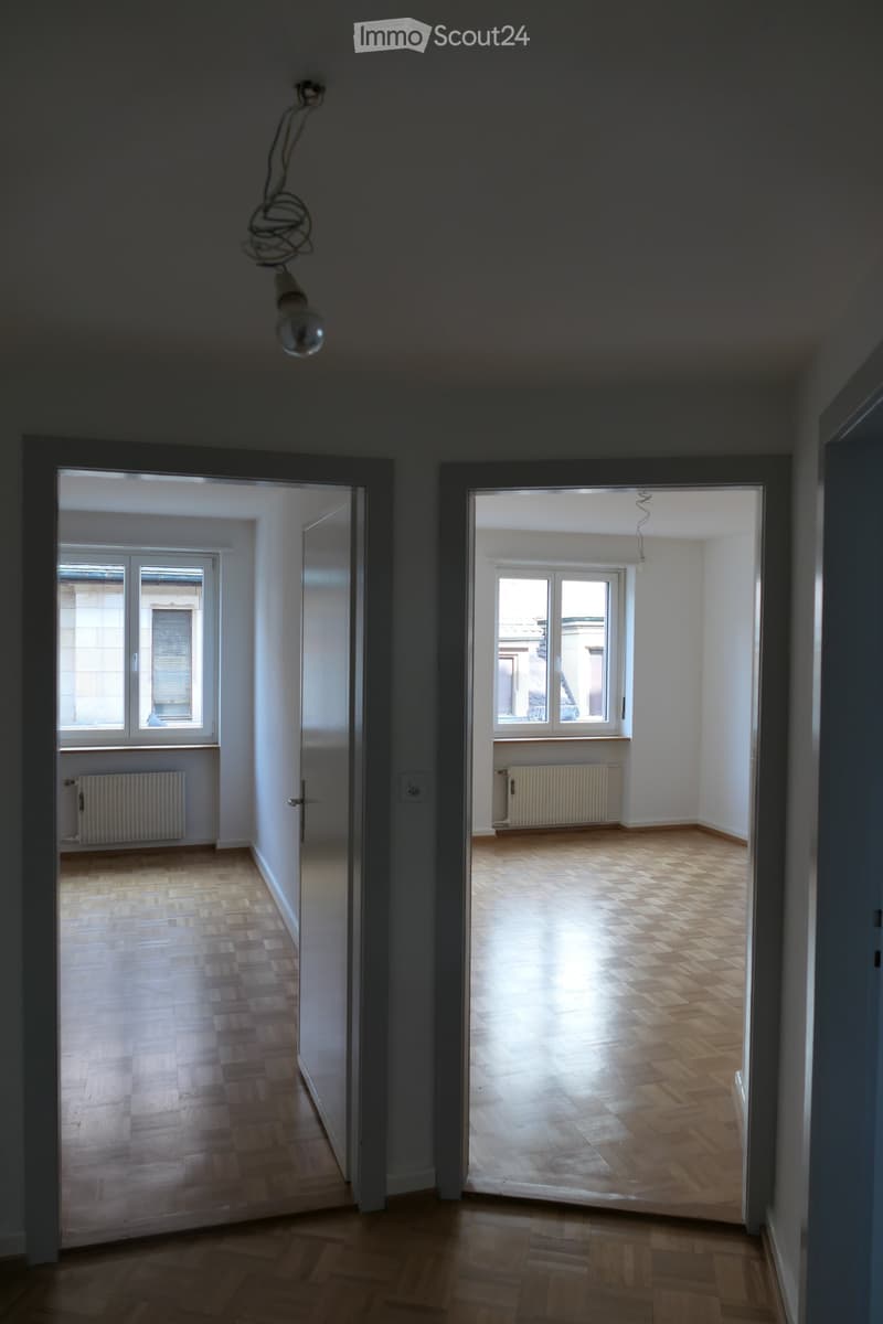 Empty room, wooden floor, white walls, radiators under the windows, open doors.