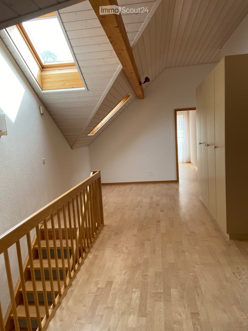 Bright, wooden-floored hallway with a staircase leading upwards, featuring a wooden railing and skylight windows.