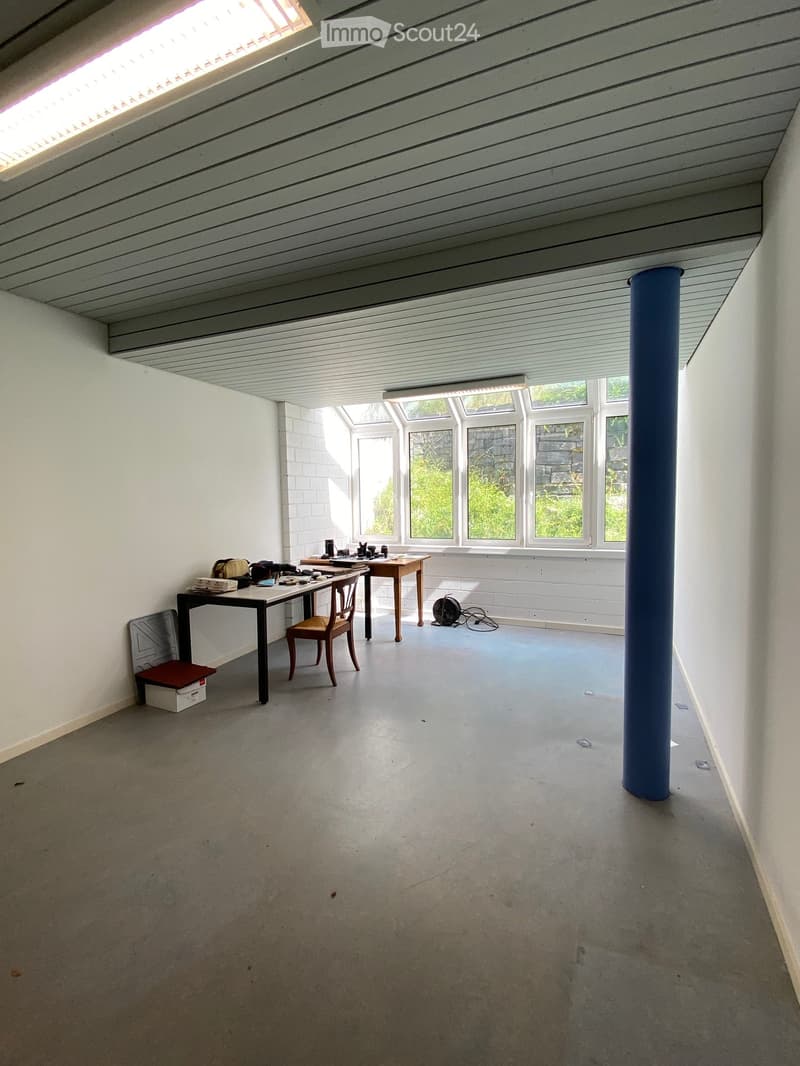 Bright, open room with concrete floor, white brick walls, large windows, and skylights. Contains a small table with chairs, a stool, and a fan.