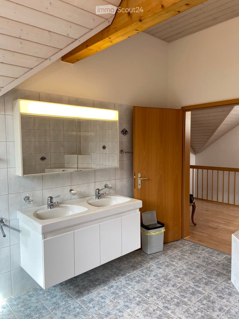 Modern bathroom with double sink, mirrored cabinet, and wooden door leading to another room.