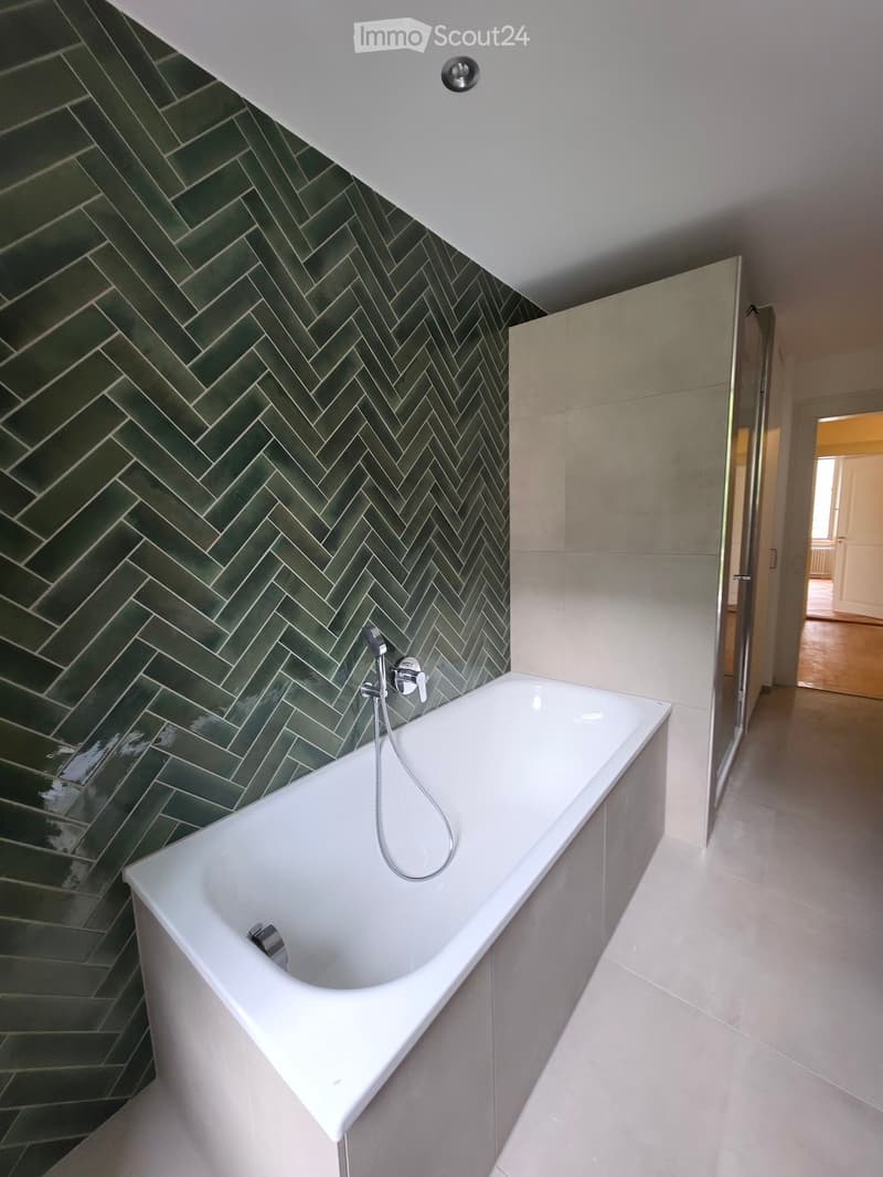 Modern bathroom with a white bathtub, green herringbone tiled walls, and a sleek faucet.