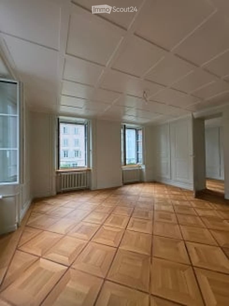 Completely empty room with wooden flooring, white walls, and large windows. No furniture or equipment.