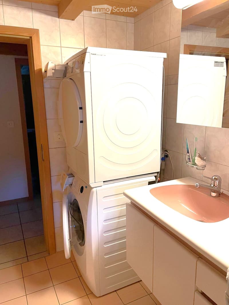 Compact bathroom with a white washing machine, a sink with a faucet, and a toothbrush holder with toothbrushes and toothpaste.