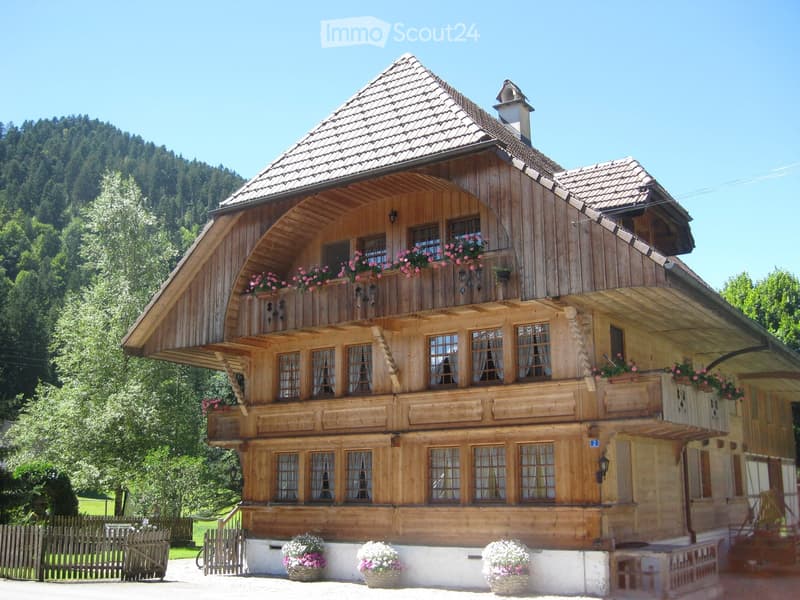 Traditional wooden house with a steep roof, multiple windows, and flower boxes on the balcony and ground level.