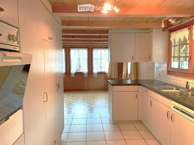 Bright kitchen with white cabinets, tiled floor, and a black countertop. Features a sink with a faucet, an oven, and large windows with curtains.
