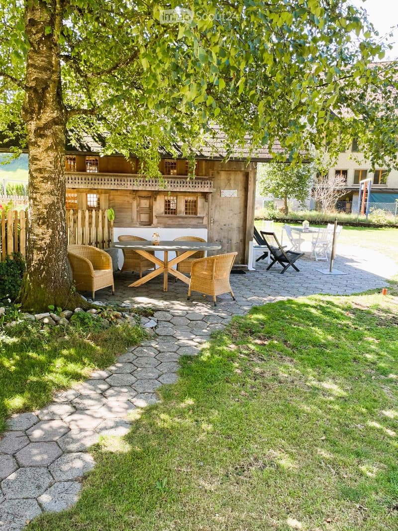 Outdoor seating area with a table and chairs, surrounded by a grassy lawn and a stone pathway.