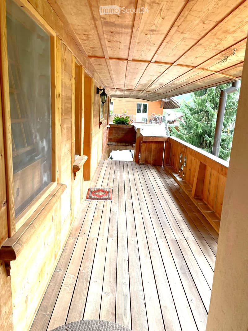 Wooden balcony with a wooden floor, wooden railings, and a small rug in the center.