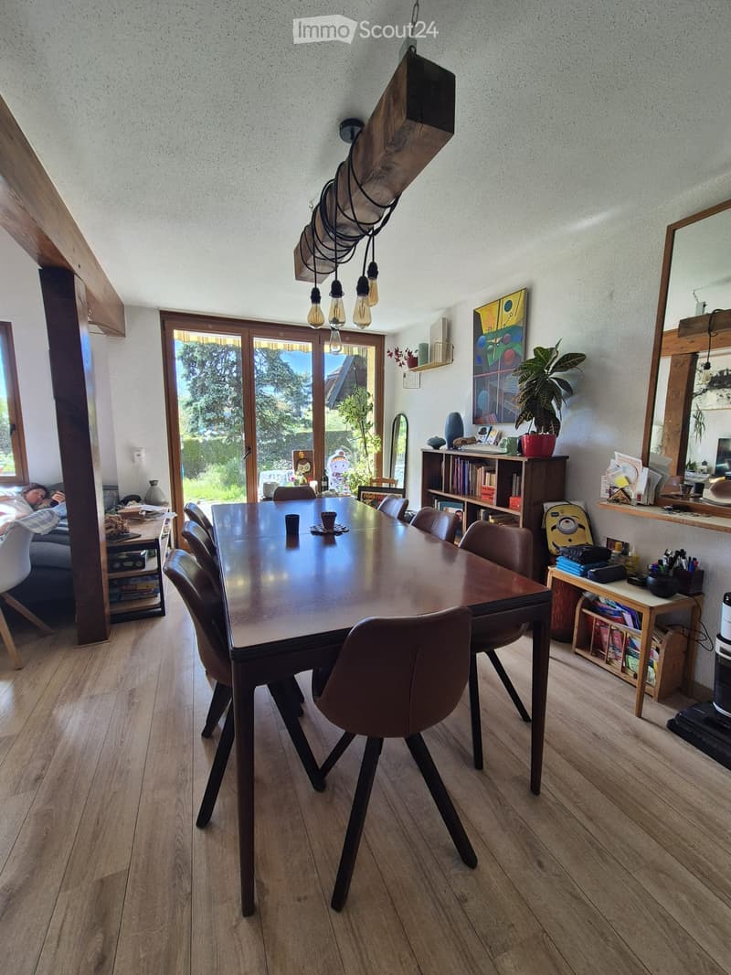 Dining room with a modern wooden dining table and chairs, a bookshelf, a large mirror, and a view of the garden through large windows.