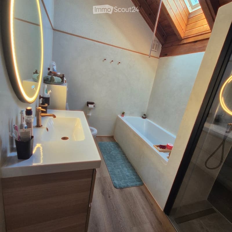 Modern bathroom with a large sink, mirror, bathtub, and toilet. Features wooden flooring and a skylight window.