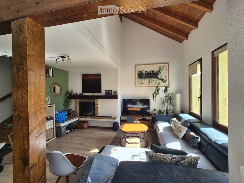 Cozy living room with exposed wooden beams, fireplace, large windows, sofa, coffee table, and television.