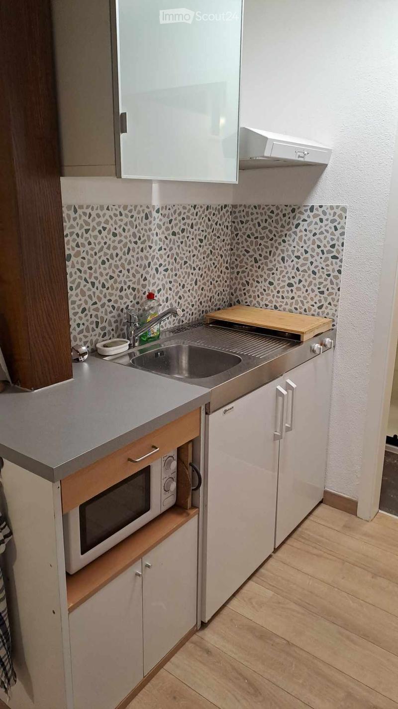 Compact kitchen with white cabinets, a stainless steel sink, microwave, and a wooden cutting board on the counter.