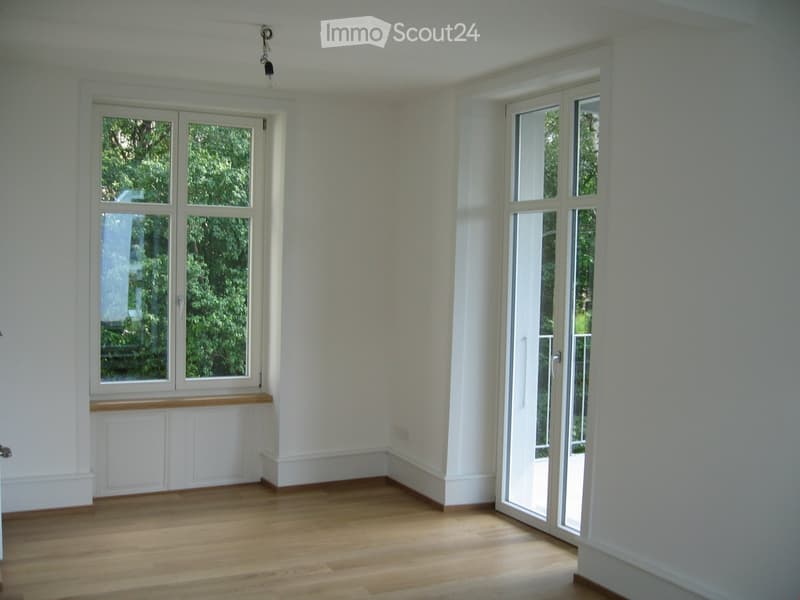 Empty room with wooden flooring, white walls, large windows, and a sliding glass door leading outside.