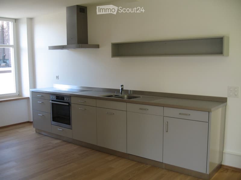 Modern kitchen with grey cabinets, stainless steel appliances, and a wooden floor.