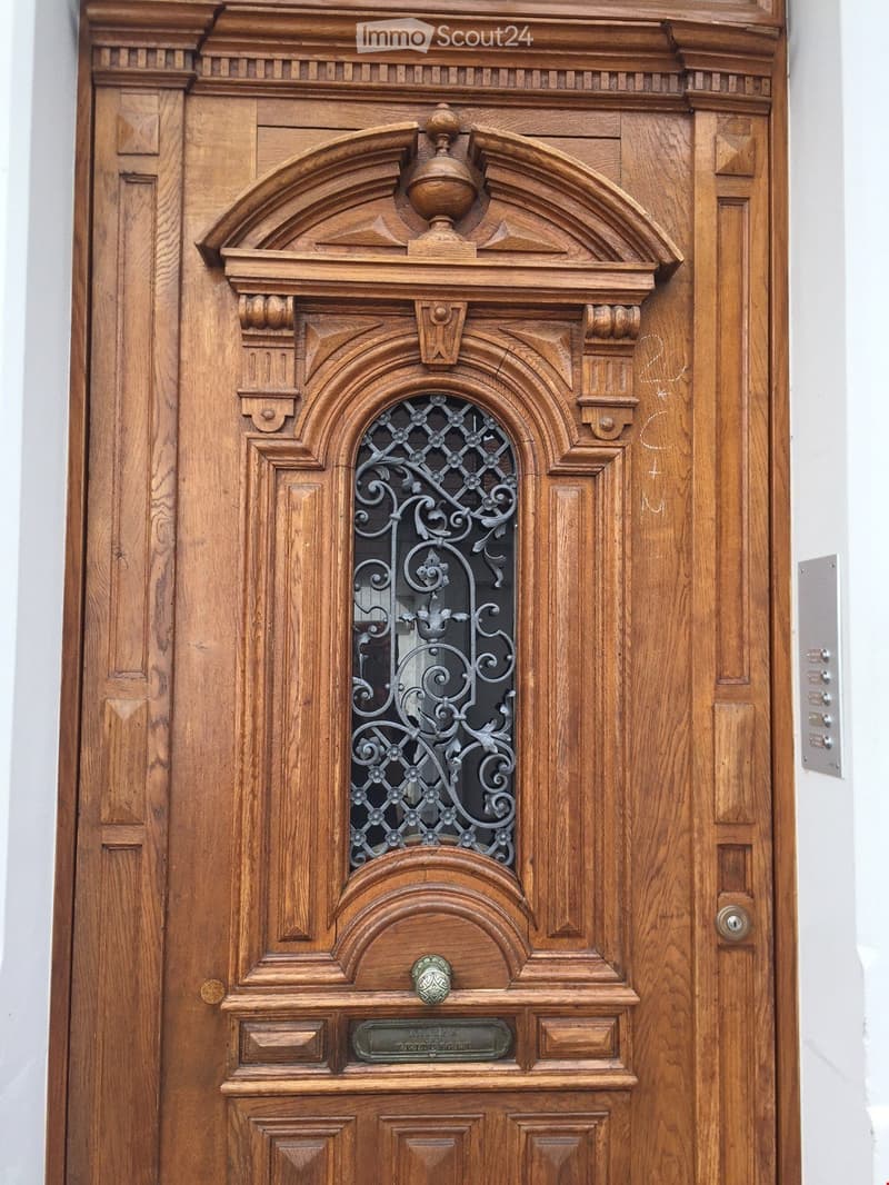 Ornate wooden door with decorative carvings, a small arched window with wrought iron grillwork, and a nameplate below the handle.