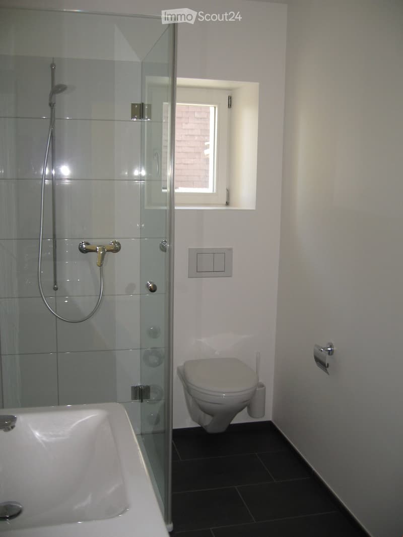 Modern bathroom with a bathtub, toilet, glass-enclosed shower, and a small window above the toilet.