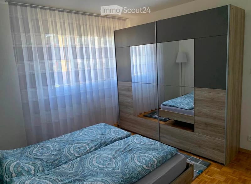 Modern bedroom with two single beds, a large mirrored wardrobe, and a lamp on the floor.
