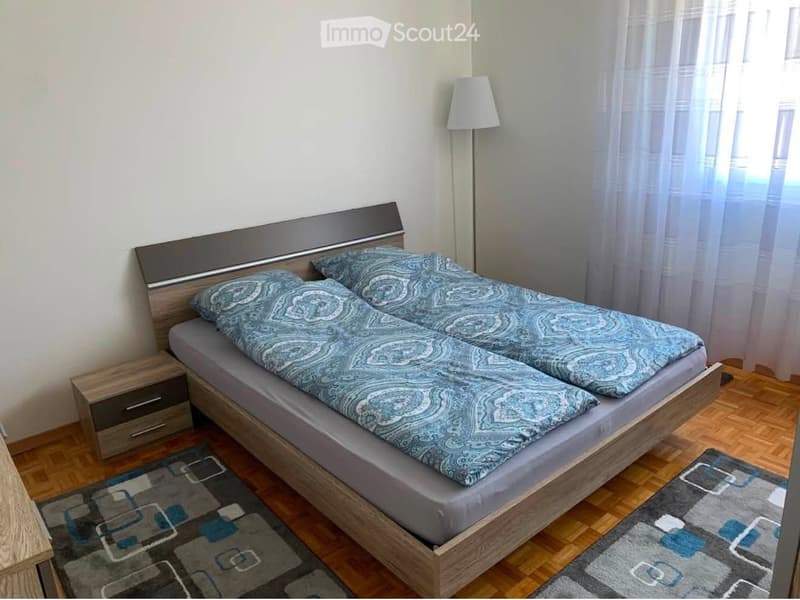 Bedroom with a double bed, nightstand, lamp, and a patterned rug on the floor.