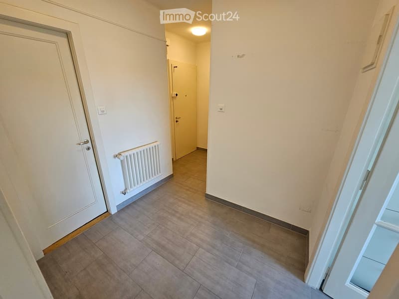 Empty hallway with tiled floor, white walls, radiator, and two doors.