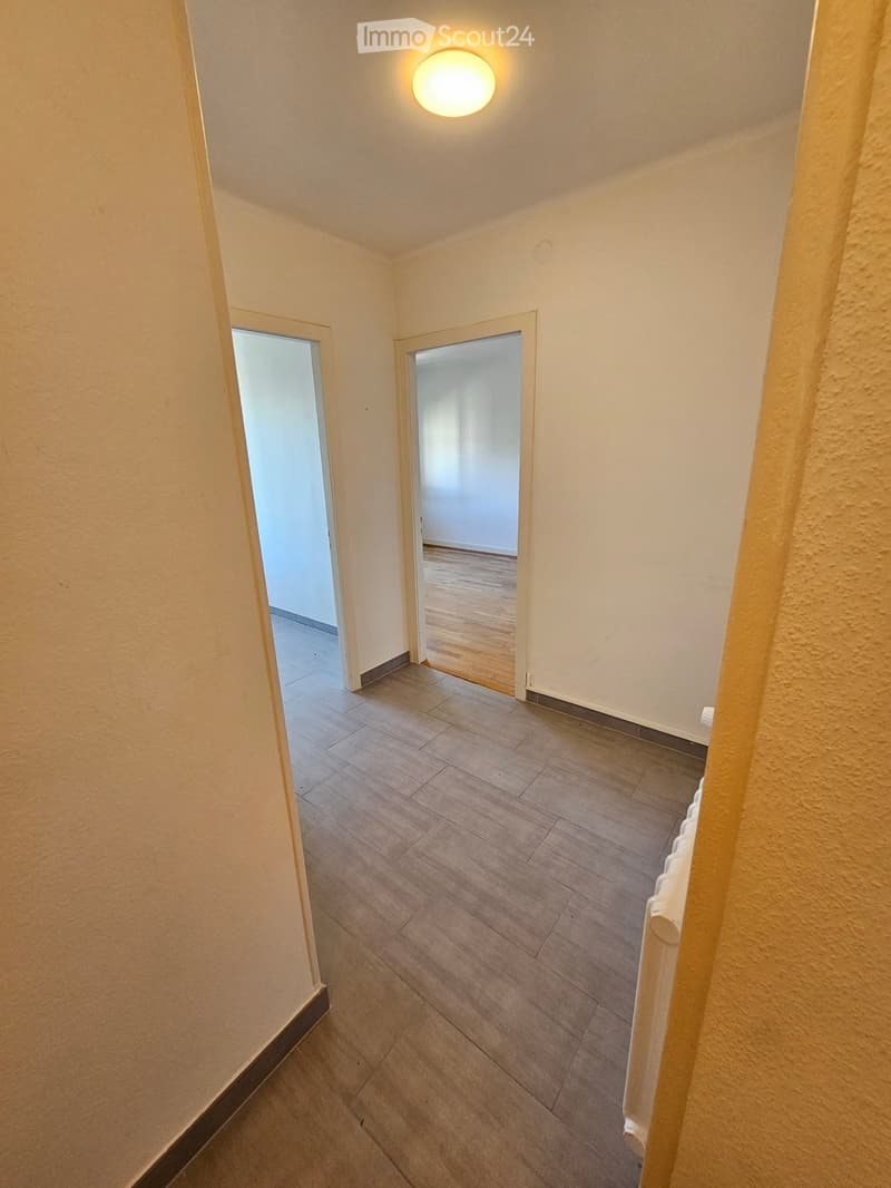 Empty hallway with wooden flooring, white walls, and two open doors leading to other rooms.