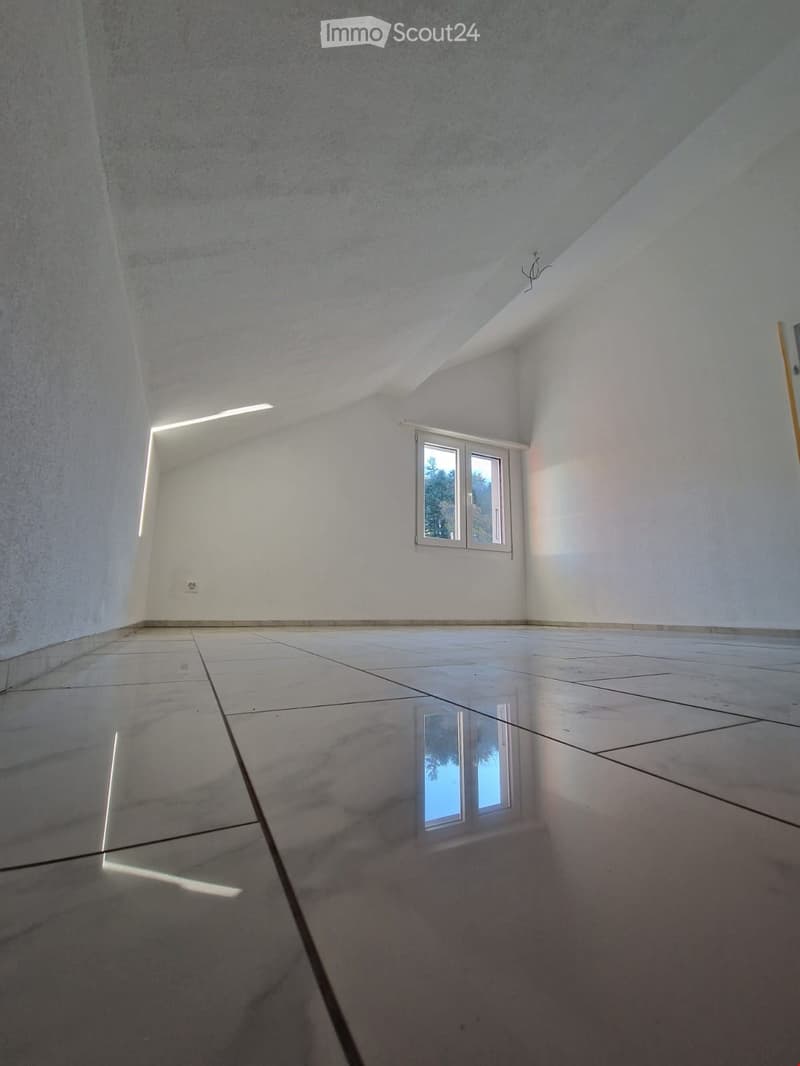 Empty room with white walls, white tiled floor, and a window with a view of trees outside.
