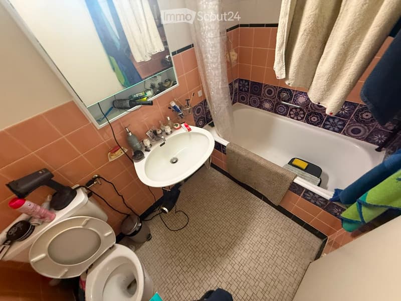 Bathroom with a toilet, sink, bathtub, mirror, and towels. The walls are tiled in orange and blue, and the floor is tiled in a small mosaic pattern.
