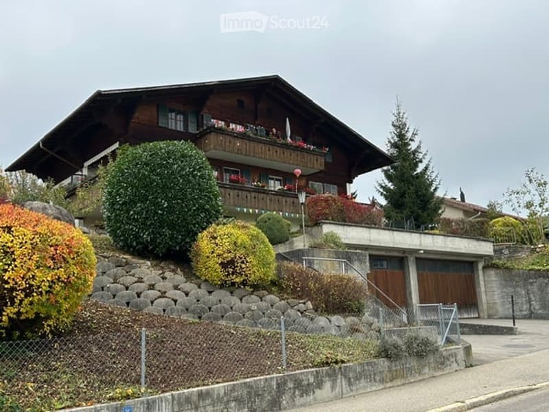 Traditional Swiss wooden house with a balcony, surrounded by well-maintained gardens and stone retaining walls.