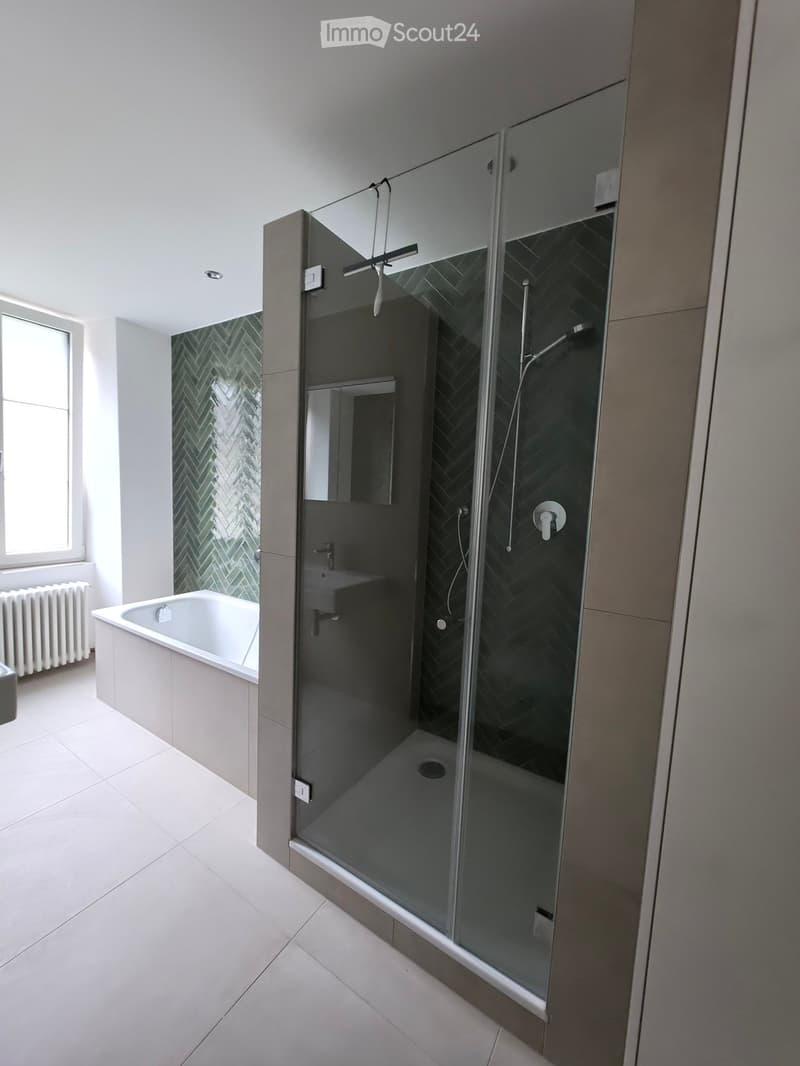 Modern bathroom with a bathtub, glass-enclosed shower, and a radiator near the window.