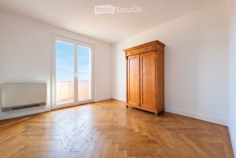 Bright, unfurnished room with wooden flooring, large window offering a view, and a wooden wardrobe.