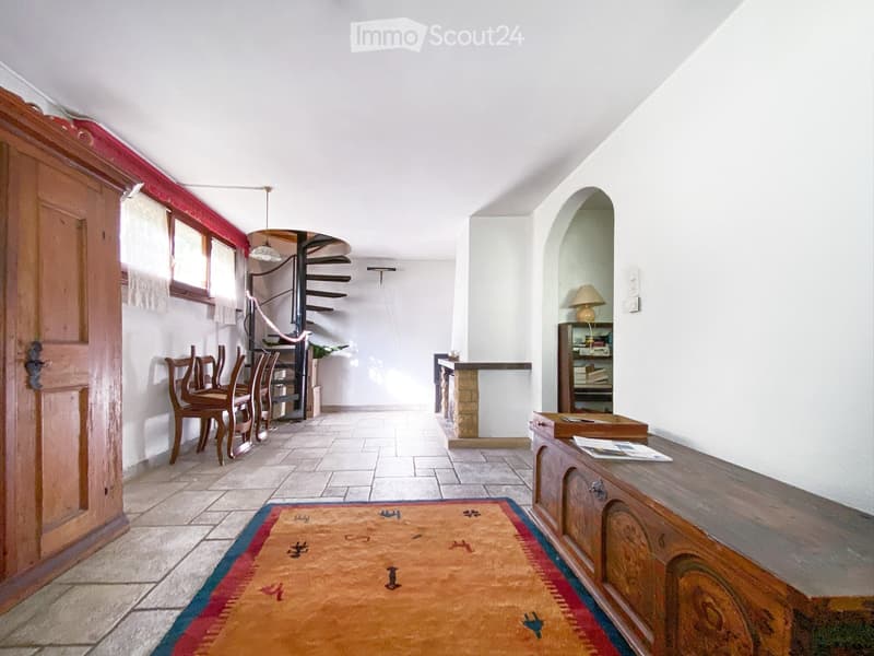 a corridor with stone flooring, a wooden door, a rug, a dining set with chairs, a spiral staircase, and a fireplace