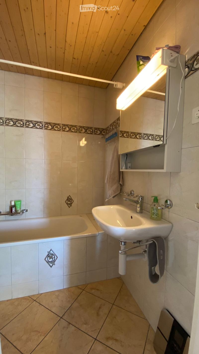 Bathroom with a bathtub, sink, mirror, and tiled walls. Features a wooden slanted ceiling and a towel hanging on the side.