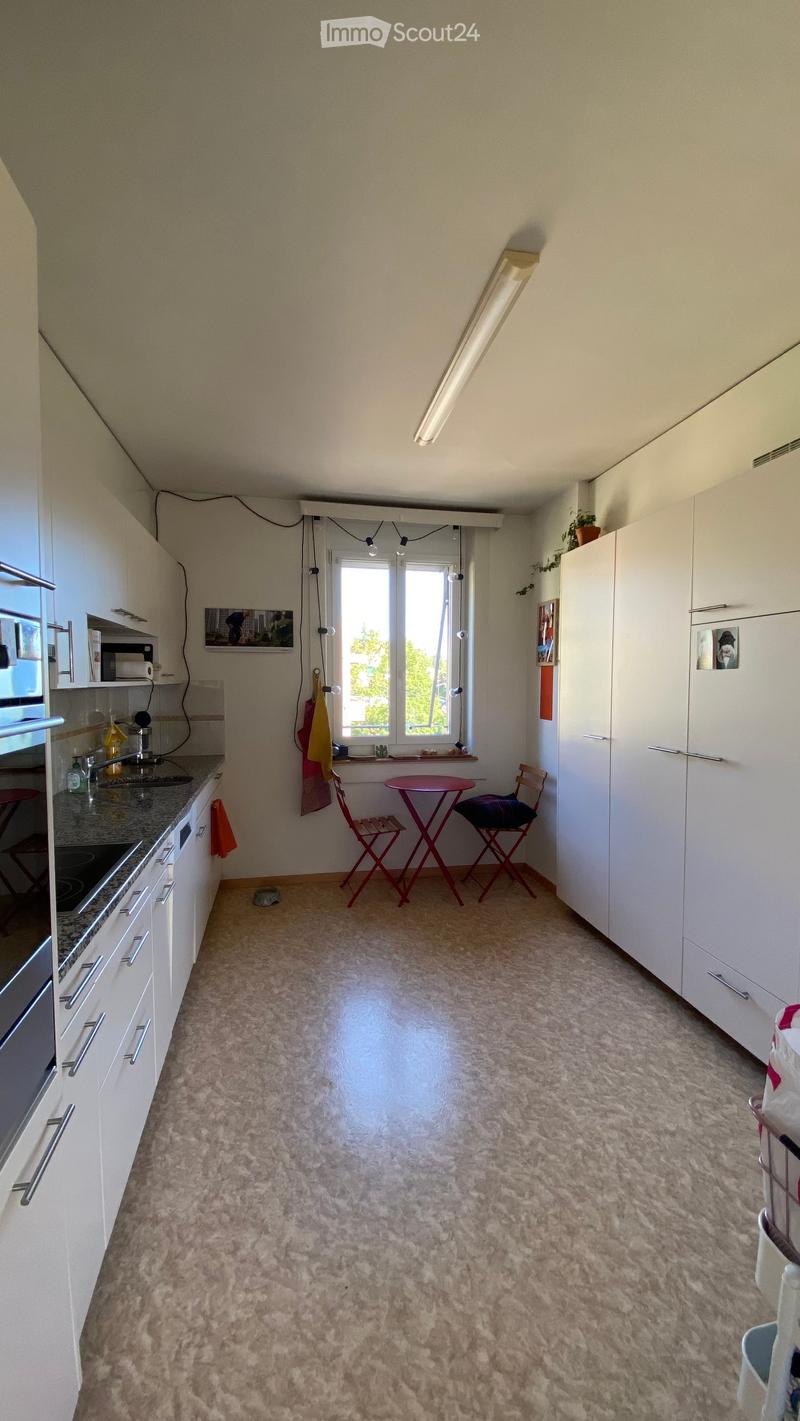 A small, well-lit kitchen with white cabinets, a granite countertop, and a small dining area with a red table and chairs.