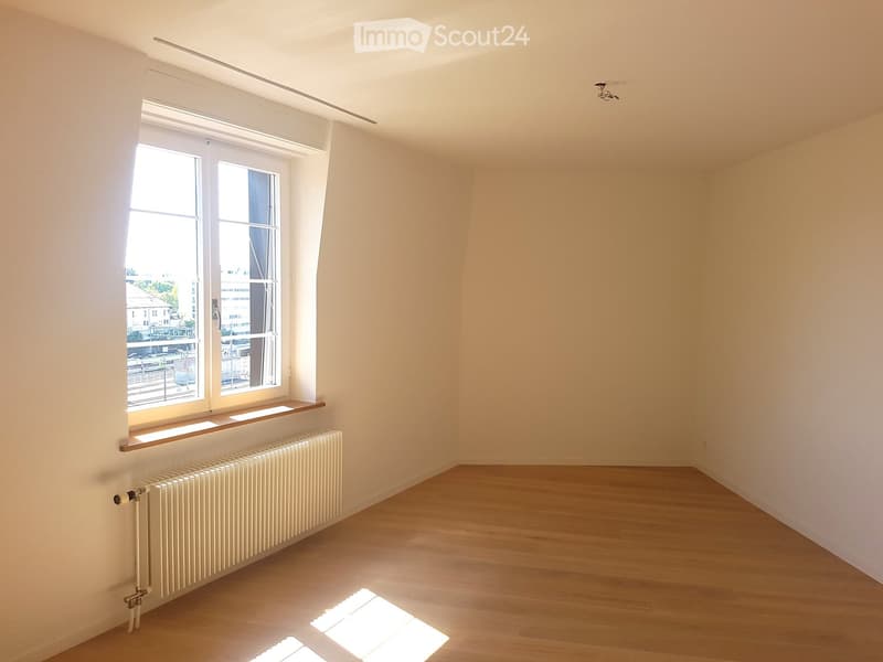 Empty room with wooden flooring, white walls, large window with radiator below, and bright natural light.