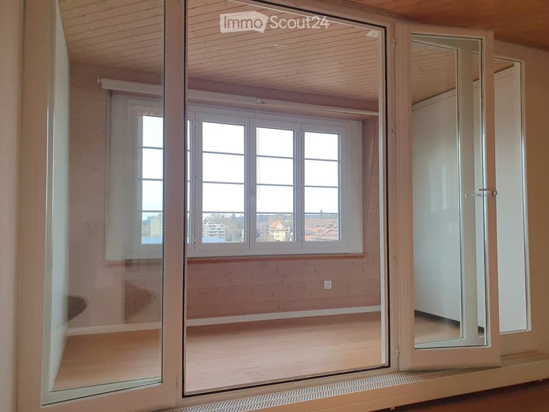 Empty room with wooden walls and ceiling, large windows, and a view of the cityscape.