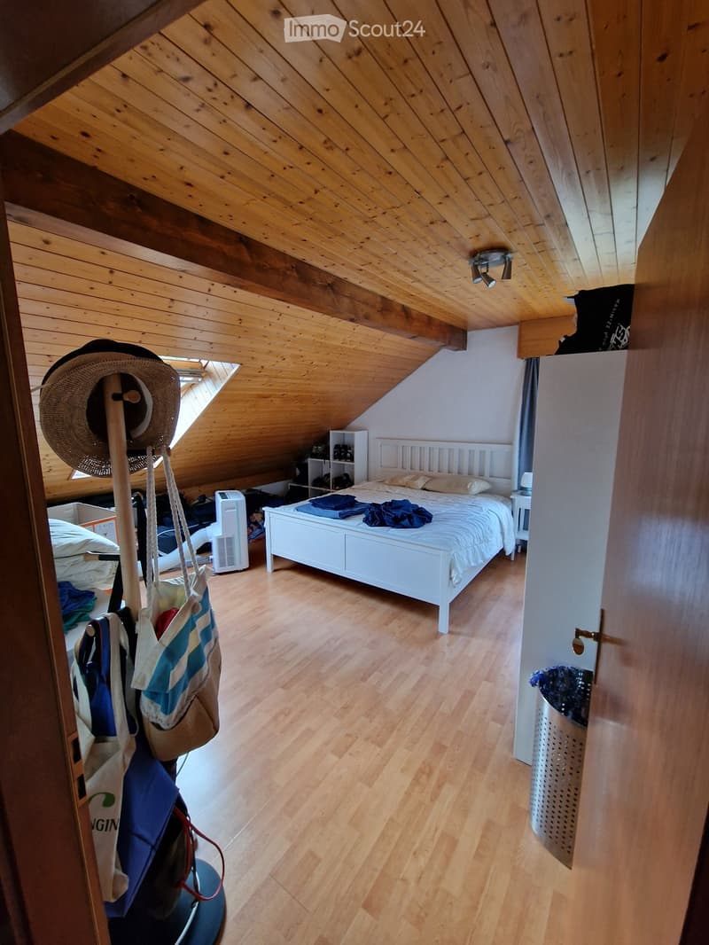 Cozy attic bedroom with wooden slanted ceilings, hardwood floors, white bed, nightstand, hat rack, and air purifier.