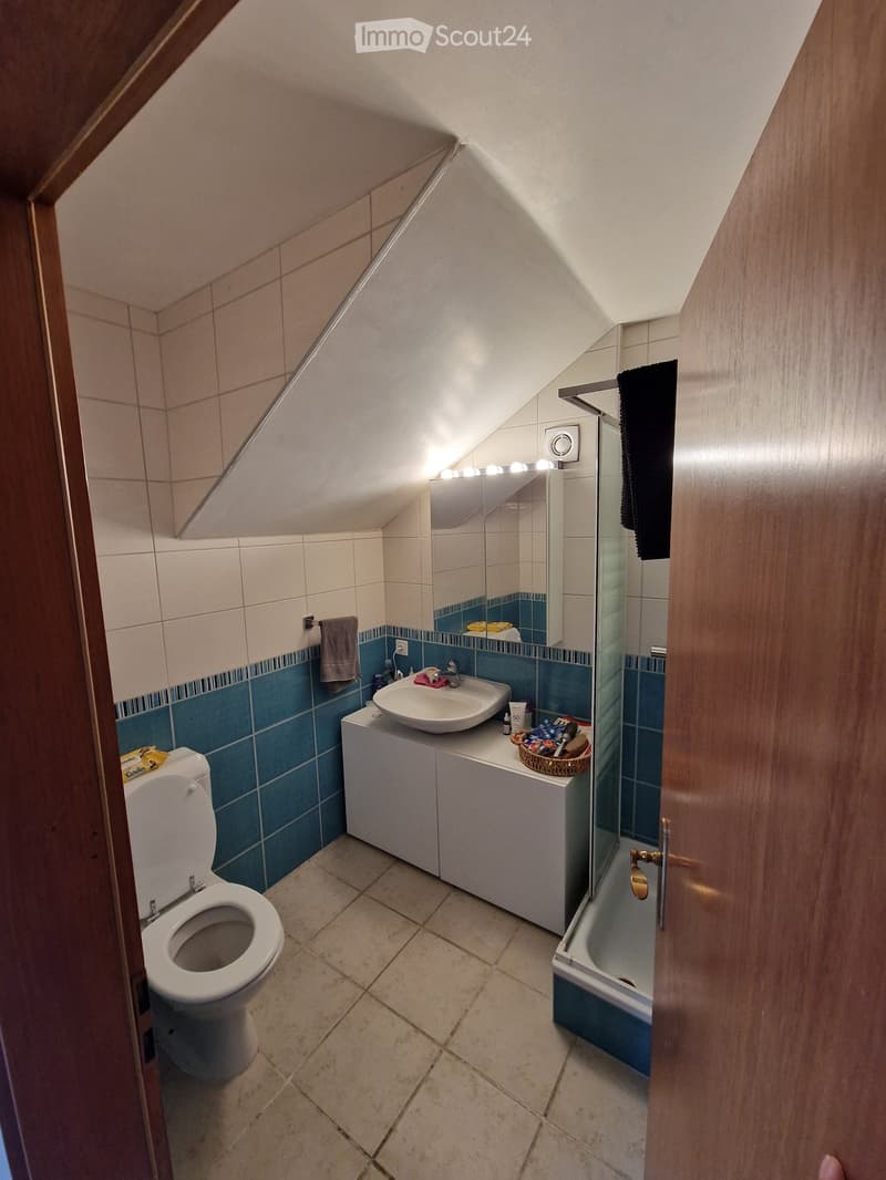 Bathroom with a toilet, sink, mirror, and bathtub. The walls are tiled in blue and beige, and there is a small cabinet under the sink.