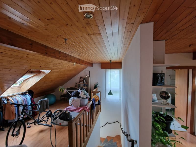 Attic room with wooden ceiling and slanted roof, featuring a bicycle, ironing board, ball, shelves with picture frames, and a lamp.