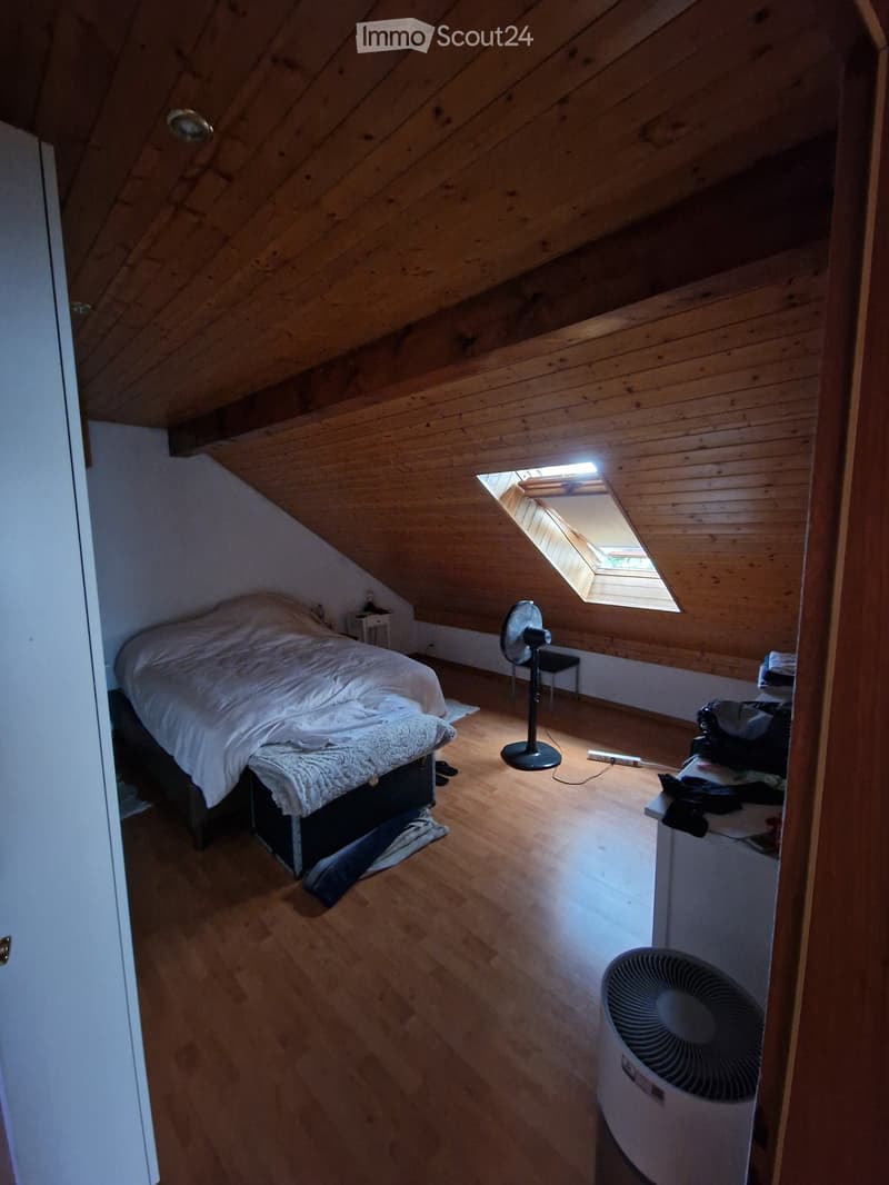 Cozy attic bedroom with wooden slanted ceilings, skylight window, bed, fan, nightstand, and mirror.