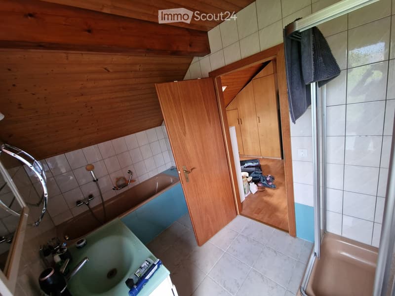 Bathroom with a bathtub, sink, and shower area. Wooden cabinets and tiled walls are visible, along with a towel hanging on the door.