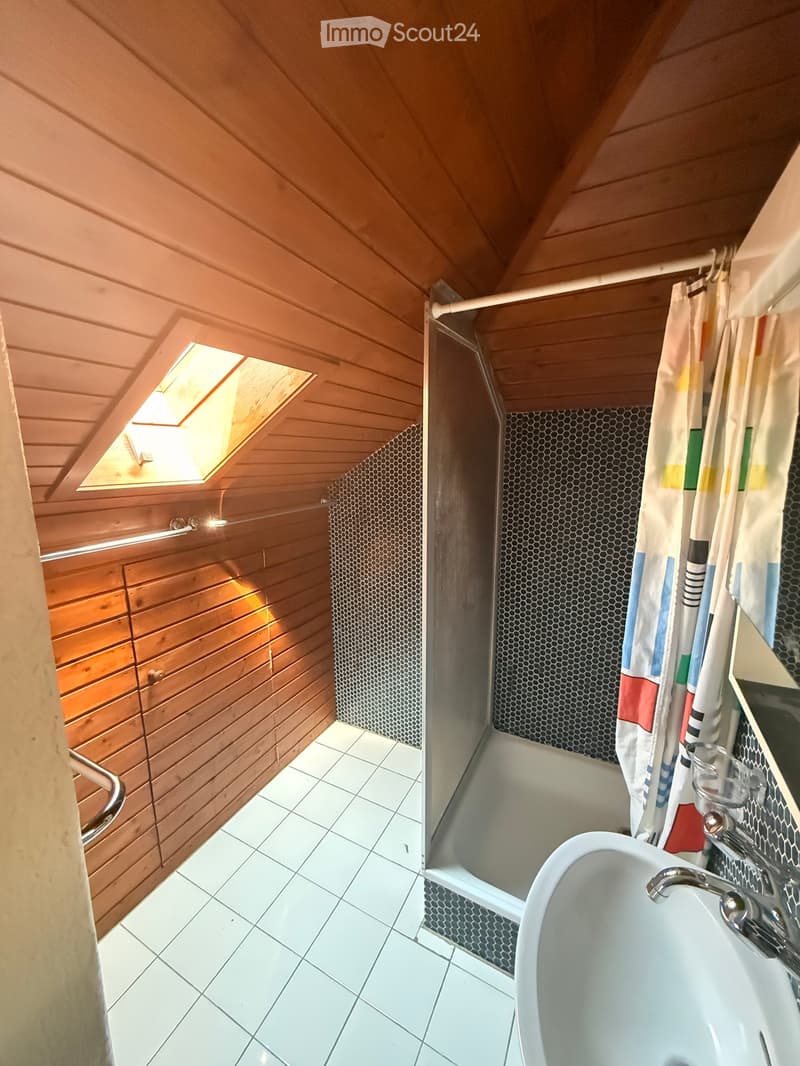 Bathroom with a bathtub, shower stall, and a window letting in natural light. The walls are wooden, and the floor is tiled.