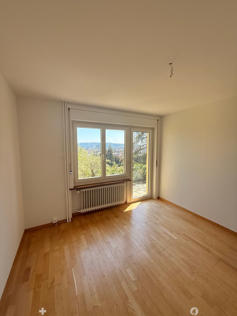 Empty room with wooden flooring, large windows, radiator, and white walls.