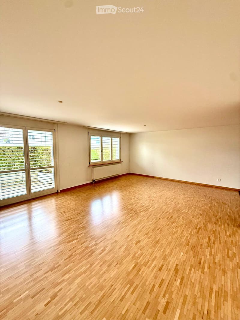 Empty room with wooden flooring, large windows, and a radiator. No furniture or equipment present.
