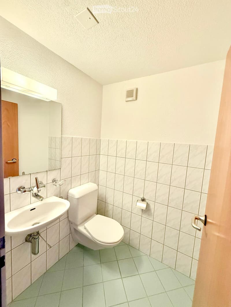 Small bathroom with white tiled walls, green tiled floor, toilet, sink, and mirror.