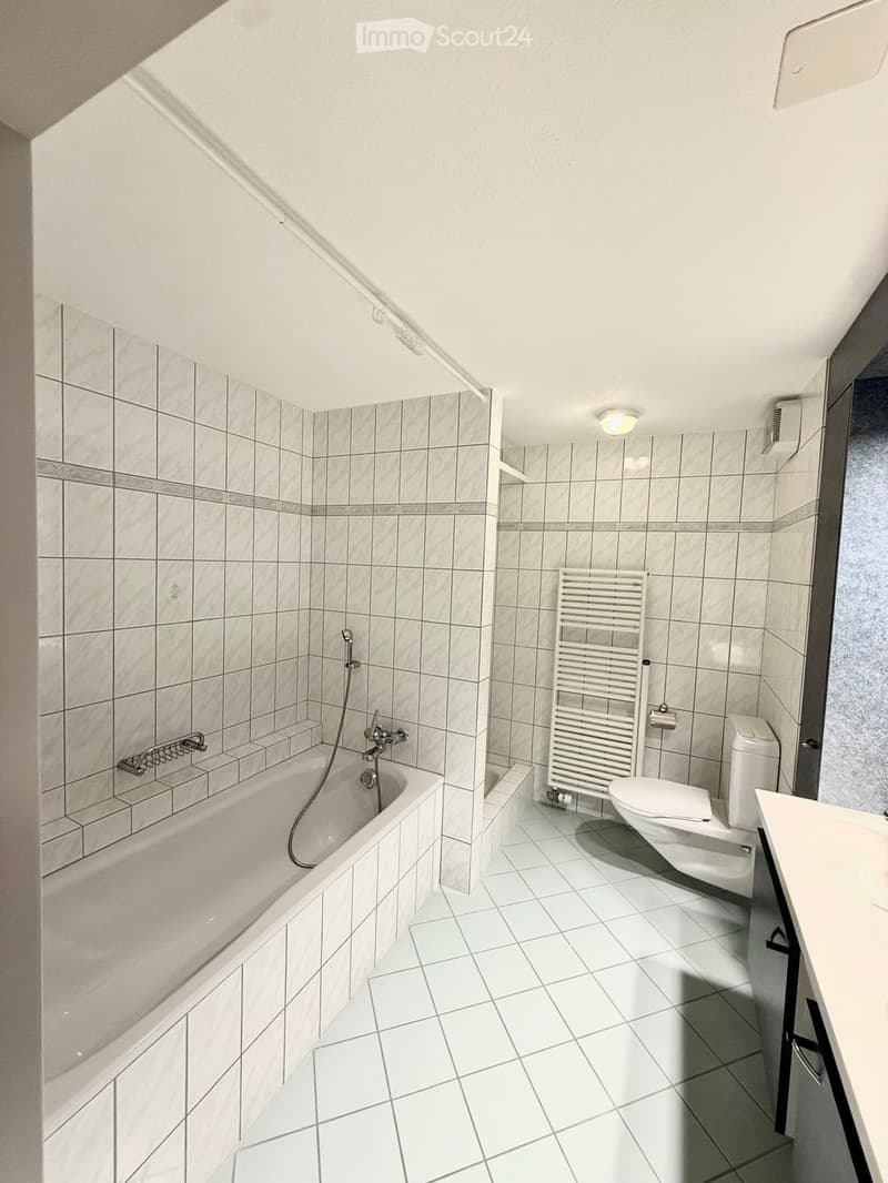 Modern bathroom with a bathtub, toilet, radiator, and tiled walls and floor.