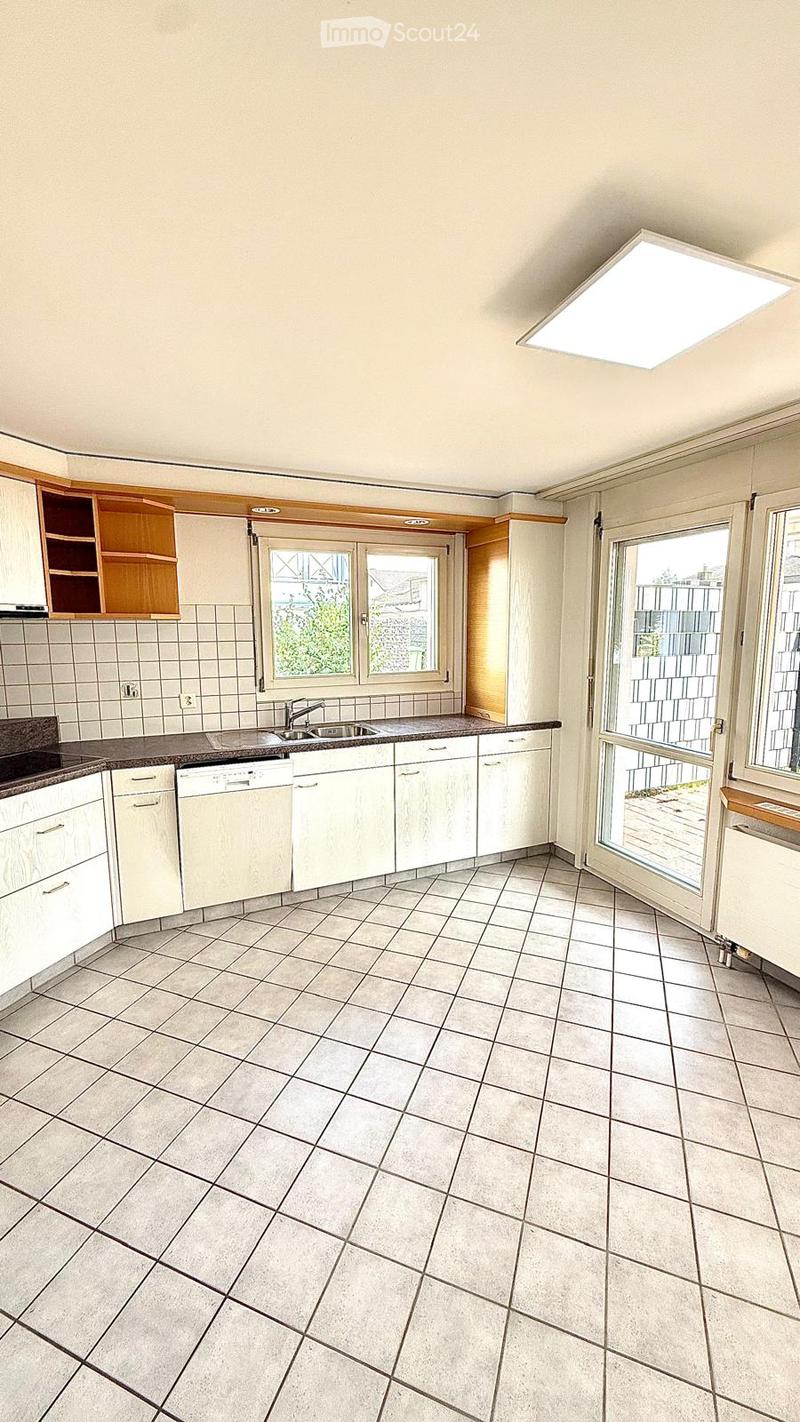 Empty kitchen with white tiled walls, tiled floor, white cabinets, sink, and dishwasher.