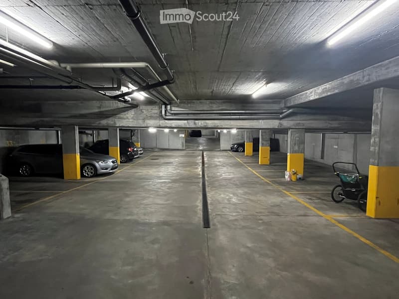 Underground parking area with several parked cars, concrete pillars, and yellow markings on the floor.