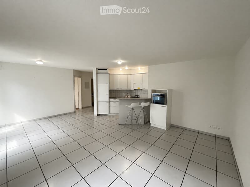 A modern kitchen with white cabinets, a refrigerator, an oven, and two stools at the counter. The floor is tiled, and the walls are painted white.