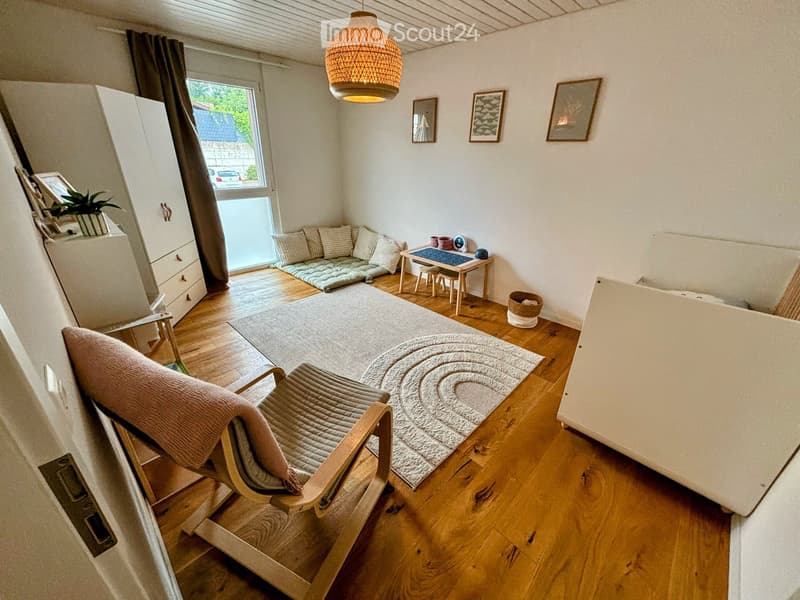 Cozy living room with wooden flooring, a sofa, a chair, a small table with stools, a cabinet, and a hanging lamp.