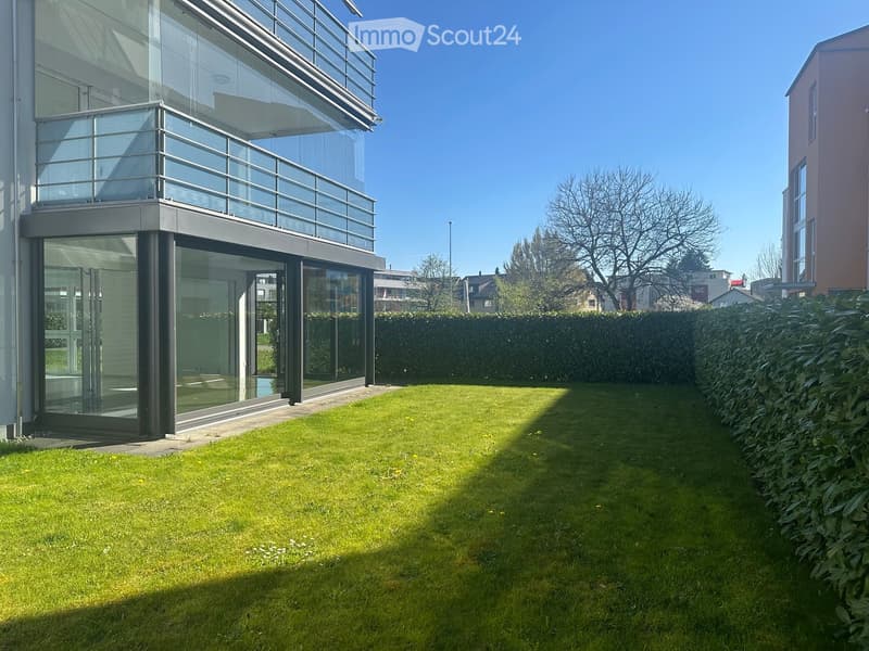 Garden / Outdoor Area. Well-maintained lawn with small yellow flowers, surrounded by a neatly trimmed hedge and a modern building with large glass windows and a balcony.