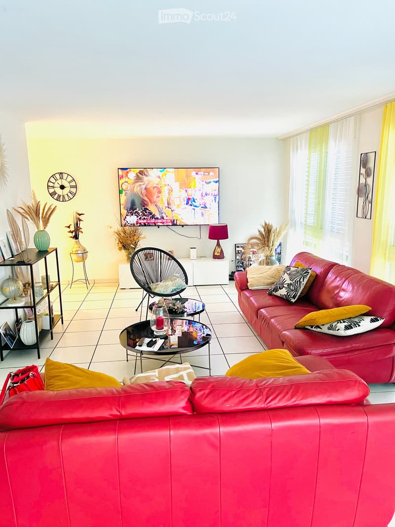 Modern living room with red leather sofa, coffee table, TV, decorative vases, and a wall-mounted clock.