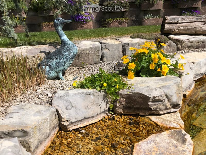 Garden area with a decorative bronze duck sculpture, yellow flowers, rocks, and a small water feature.